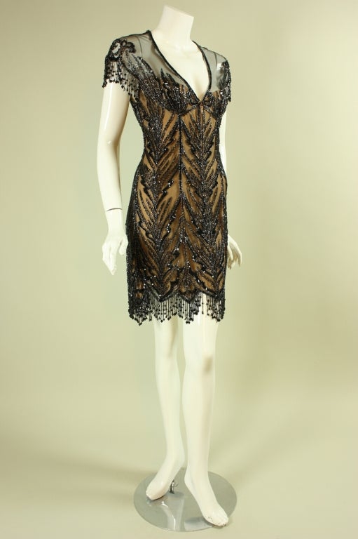 Show-stopping cocktail dress from Bob Mackie dates to the 1990's and retailed at Saks Fifth Avenue.  It features a deep v-neck with beaded trim, cap sleeves with beaded fringe, and matching beading at the hem.  Nude lining contrasts with the areas