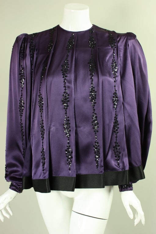 Pleated silk blouse from James Galanos is made of plum-colored silk charmeuse with vertical rows of black sequins sewn on.  Round neck.  Long sleeves with snap cuff.  Band of black silk trims the hem.  Center back snap closure.  Unlined.

No size