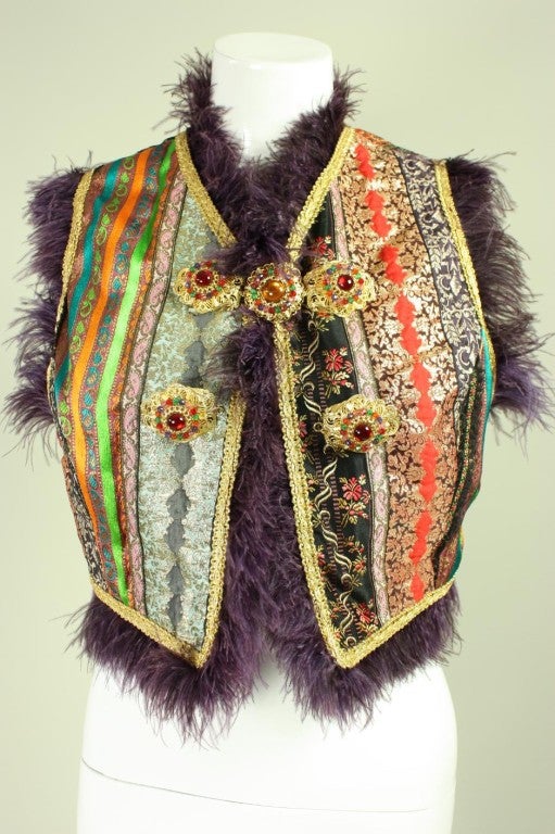 Colorful vest from Dolce & Gabbana is made of bands of ribbons in contrasting colors and patterns.  Plum-colored marabou feather trim.  Center front gold-toned metal closure has red glass cabochons surrounded by multi-colored faceted beads. 