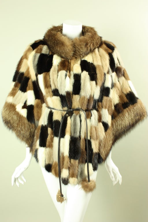 Vintage Elsa Schiaparelli capelet dates to the 1970's and is made of a mixture of cream, light brown, and dark brown furs.  Stand collar.  Wide sleeves.  Fully lined.  Brown faux leather tie with fur pompoms on the ends.