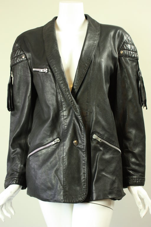 Claude Montana for Idéal Cuir black leather jacket dates to the 1980's through 1990's.  It features a narrow shawl lapel, three zippered pockets, and a center back vent.  Long sleeves have tassel detail at upper arm.  Lined.