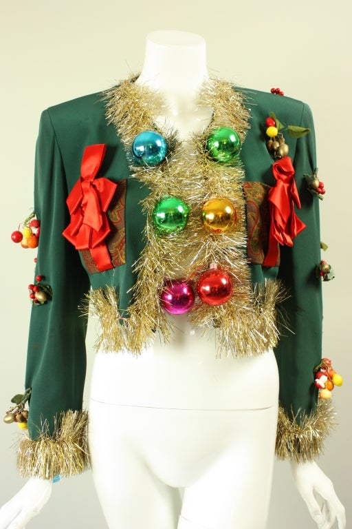 Iconic and rare Christmas tree jacket from Moschino Couture dates to the 1990's.  It is made  of forest green gabardine that is trimmed with gold and silver tinsel.  Multicolored spherical bulbs run down the center front and are grouped at the
