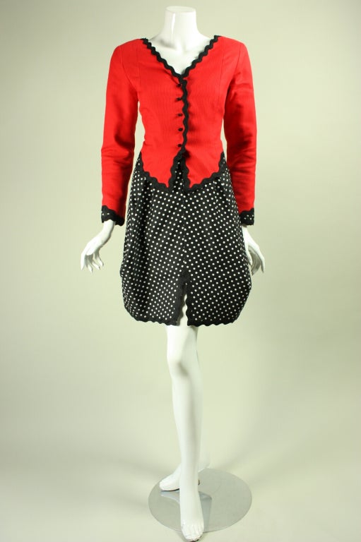 Fun skirt suit from Geoffrey Beene is made of cotton pique trimmed with thick black rickrack.  Single-breasted jacket is shaped through paneling and features areas at the cuffs and center back neck where coordinating polka-dotted fabric was