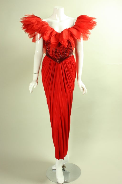 Vintage Ruben Panis red jersey gown dates to the 1980's.  The fitted bodice features off-the-shoulder sleeves that are comprised of multiple layers of fabric that resemble petals.  Beads extend up from the waist like flames.  Full-length skirt is