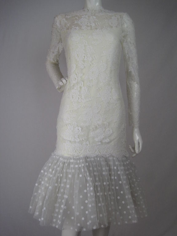 White lace dress with fishtail bottom.  Long sleeves are unlined, have scalloped cuffs with double snaps.  Scalloped boat neck.  Cream-colored crepe under lace.  Flocked netting fishtail is tightly gathered with eight layers of tulle underneath. 