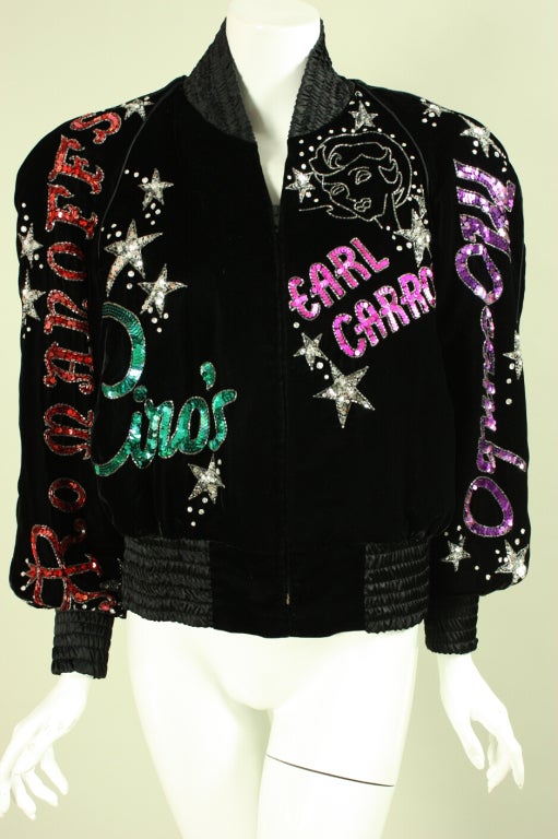 Totally unique black velvet bomber jacket from Bob Mackie features the names of famous Los Angeles nightclubs in sequins, beading, and rhinestones. It has black satin elasticized collar, cuffs, and waistband.  Slant pockets.  Lined.  Center front