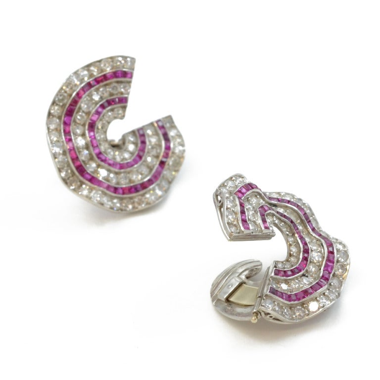 A pair of wavy c-scroll ear clips, callibre set with rubies and diamonds. Mounted in platinum. French, circa 1920.