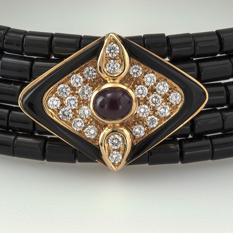 This wonderful modern collar is made with 18kt yellow gold and designed as five horizontal courses of tubular black onyx beads joined by a central plaque shaped like a pointed oval, centered by a bezel-set ruby cabochon, on a ground of diamonds,