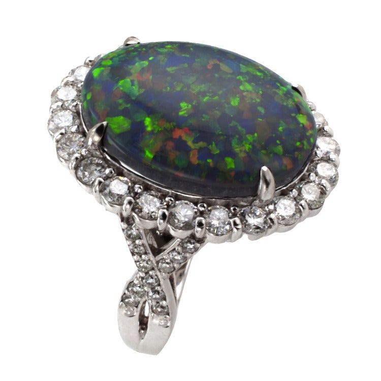 This classic styled ring, set with a solid black opal weighing  9.18 carats, exhibits a great deal of reds, blues, greens and other shades, within a conforming diamond border to the diamond-set shoulders formed by a woven motif, forty-four diamonds