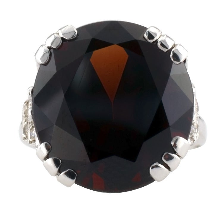 Featuring a bright and colorful oval garnet weighing 16.75 carats, between stepped shoulders set with diamonds totaling approximately 0.30 carat, mounted in platinum, Ca'1950.  Ring size 5 3/4.  And can be sized up or down. Garnet is January's