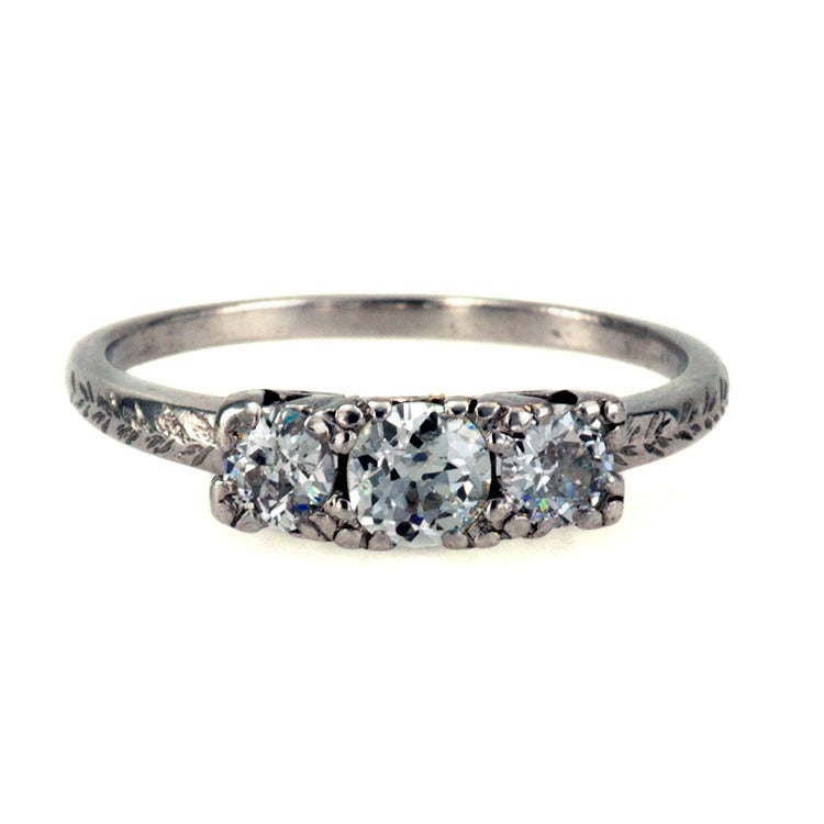 Vintage Three-Stone Diamond Ring, Circa 1930
Set in platinum with three old European-cut diamonds totaling approximately 0.60 carat, approximately H color and SI1 clarity, the shoulders decorated by chase work, and a pierced gallery formed by
