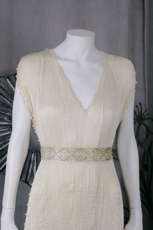 This dress is made of finely pleated off white colored silk with silk cording along side seams  and clear striped glass beads threaded through the cording. <br />
<br />
Named after a Greek classical sculpture, the Delphos Gown was a simple column