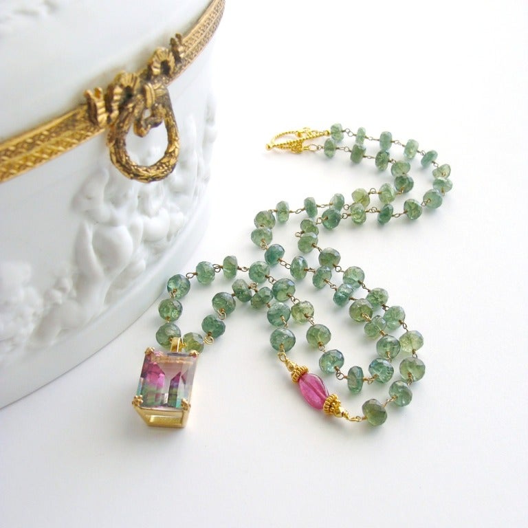 Faceted green tourmaline rondelles have been hand linked to form a classic necklace featuring a sparkling emerald cut bi-colored tourmaline topaz pendant.  An asymmetrical pink sapphire has been placed on the beaded chain to highlight the gorgeous