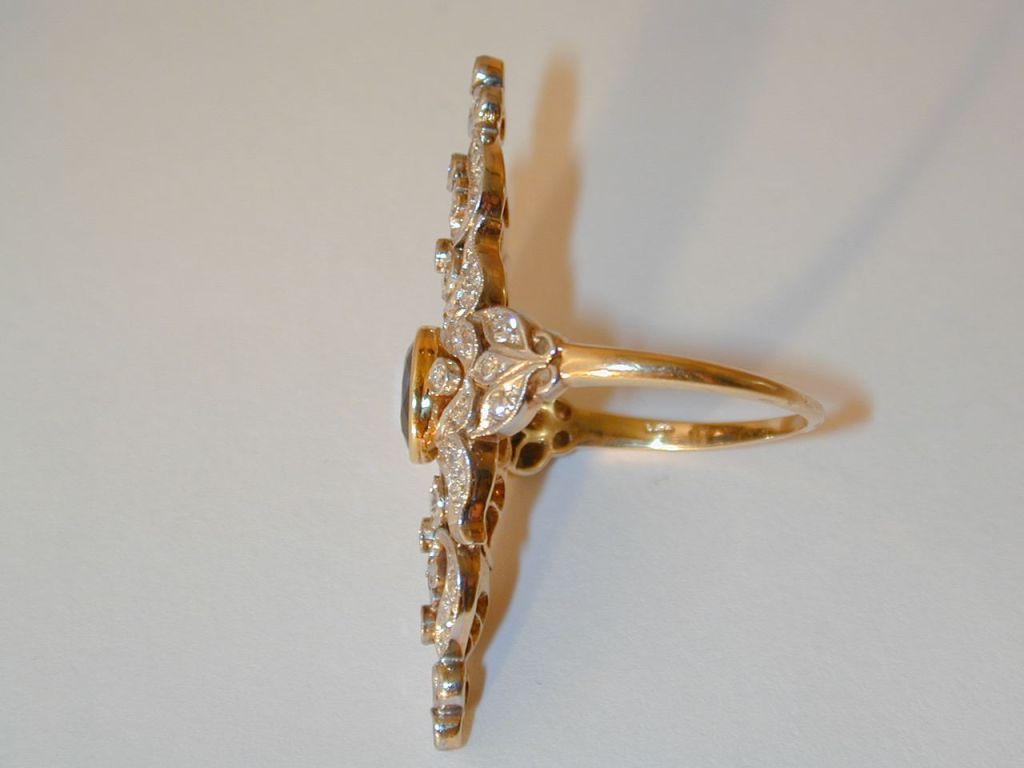 Platinum-topped 14KT yellow gold elongated, filigreed antique ring having at center a bezel-set oval faceted blue sapphire weighing approximately 1.65cts.  The lozenge-shaped top of the ring is decorated with bezel-set Old Mine Cut and single-cut