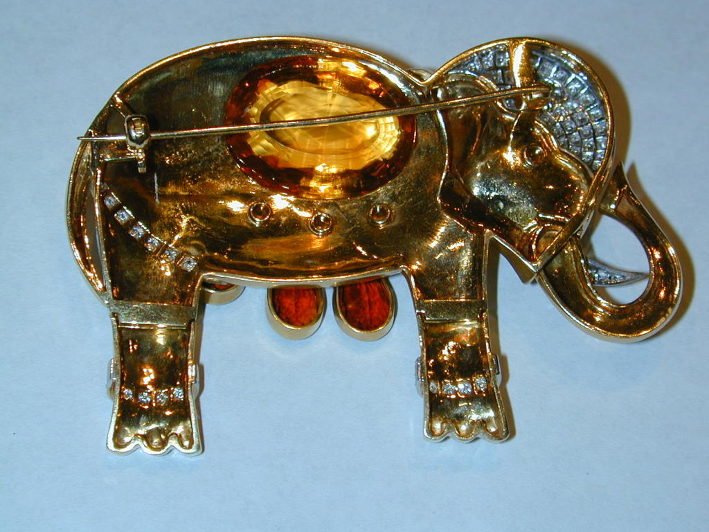 18KT matte finished yellow gold elephant brooch having a pavé diamond head dress, eye, tusk and leg bands. The legs & trunk are hinged; the saddle blanket is a large bezel-set faceted citrine set pavilion up suspending four bezel-set teardrop-shaped