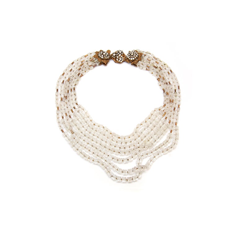 Beautiful seven strand necklace composed of clear faceted disk beads and gold toned spacer beads. Features an elaborate clasp with diamante accents