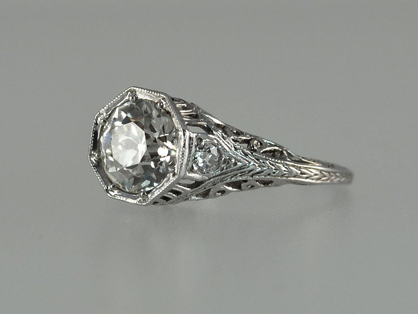 A beautiful Edwardian diamond and platinum engagement ring in an ornate filagree mounting with 2 side diamonds.  The 1.69 carat Old European Cut diamond is in an octagonal bezel setting.  The diamond is J color VS1 clarity (per EGL cert). Circa