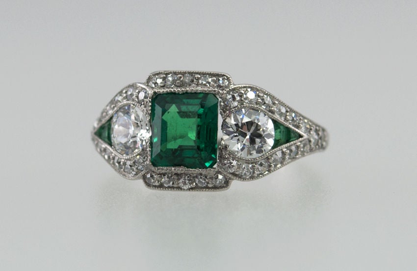 This is one of the best quality Emerald rings I've ever had! Signed JE Caldwell, the center is a spectacular color,square emerald cut emerald, 1 carat, with two little emerald accents on the sides. Also on the sides are two .33 ct old European cut