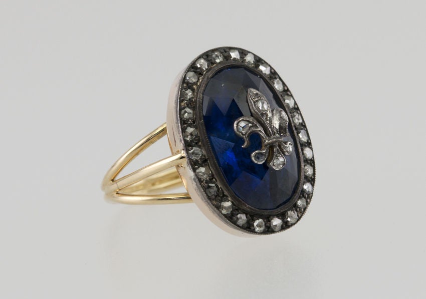 18k gold and Silver ring that has a center faceted sapphire with a silver fleur de lis encrusted with use cut diamonds, and rose cut diamonds all around the outside edge.  The back and shank are gold.  Really beautifully unusual ring!