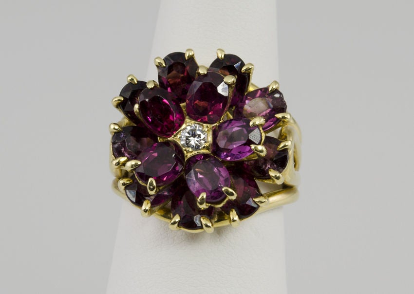 18k yellow gold ring, with two rows of purple tourmaline, and a center diamond that form a flower design.
The sides have bold curves and it is signed TIFFANY & Co.