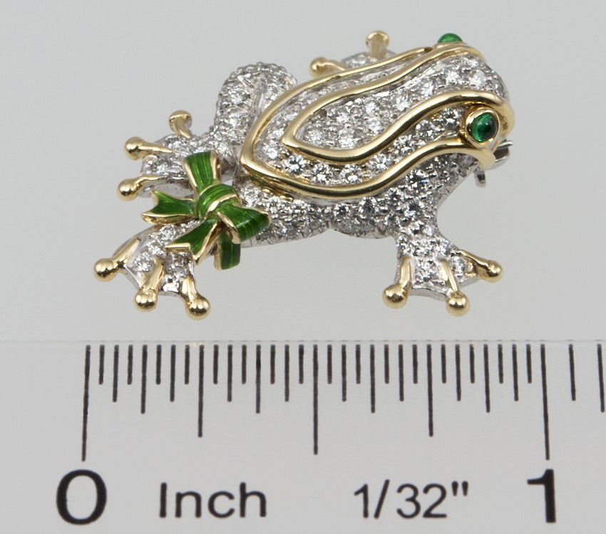 Small platinum and gold TIFFANY & CO frog pin, that has a hidden flip up bale for a chain.  It has cabochon emerald eyes and is paved with  approximately .85 cts of beautiful diamonds.  It also has a green enamel bow on the right rear leg.