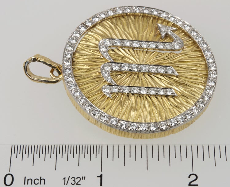 18k yellow gold textured round disc, with the astrological sign of Scorpio in diamonds.  The piece is also edged in diamonds with a total weight of 4 carats. There is a fold down bale for a large chain, and a pin back to allow it to be worn as a