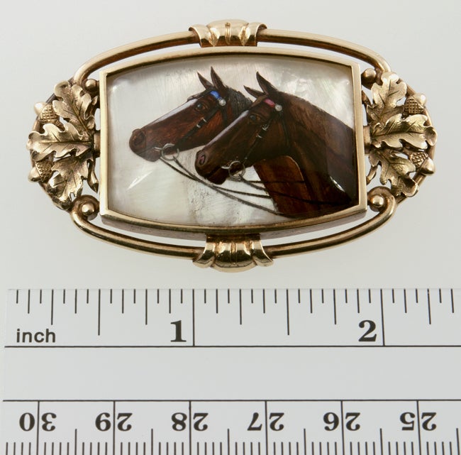Reverse painted on Mother of Pearl, under a crystal, the two horses on this brooch are very regal.  The frame is 14k yellow gold with oak leaves and acorns. The back is mother of pearl.