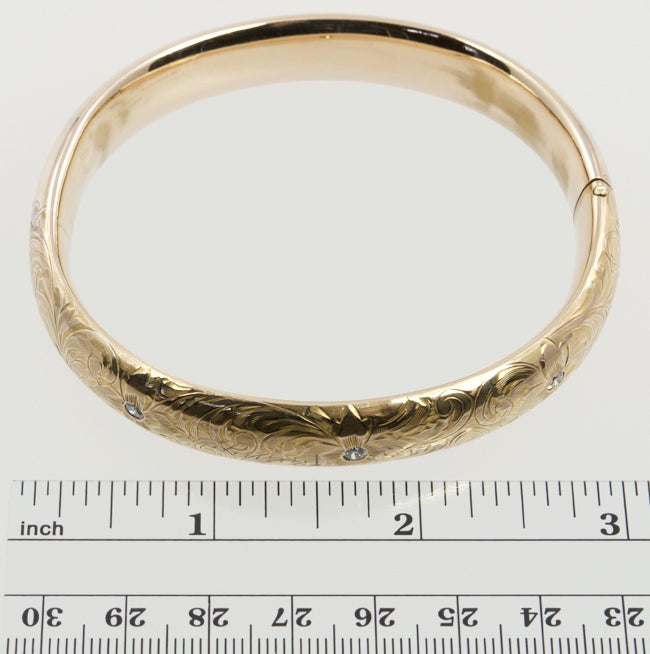 This is a rounded bangle that has been highly engraved with a floral motif.  It has an invisible hinge opening and three old european cut diamonds set into the gold. Total diamond weight approximately .33cts.