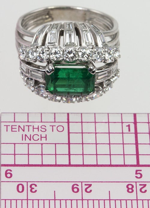 Vintage emerald and diamond bombe platinum cocktail ring circa 1950s. This beautiful ring features an approximate 1.25 carat emerald cut emerald at the center set horizontally.  Surrounding the emerald is a mix of 24 baguettes and 18 round diamonds