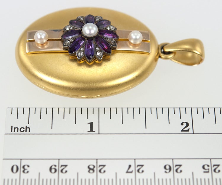 This is an oval 18k yellow gold locket, with a matte finish.  It has a a flower of amethyst and rose cut diamonds in the center, with three pearls accents.
It is signed Tiffany & Co on the back.