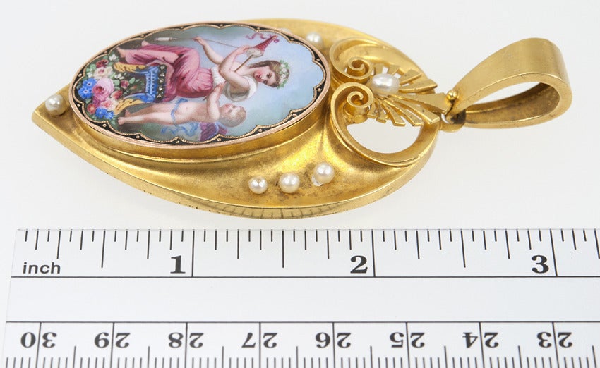 A woman and a cupid frolic in the flowers on this 18 karat painted enamel locket framed with pearls.