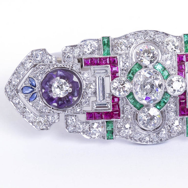 An art deco brooch with a tad more color than usual thanks to the two dainty floral designs made of hand carved petal shaped amethyst. Beautiful calibrated color gems with diamond in platinum brooch with distinct art deco styling. Center diamond