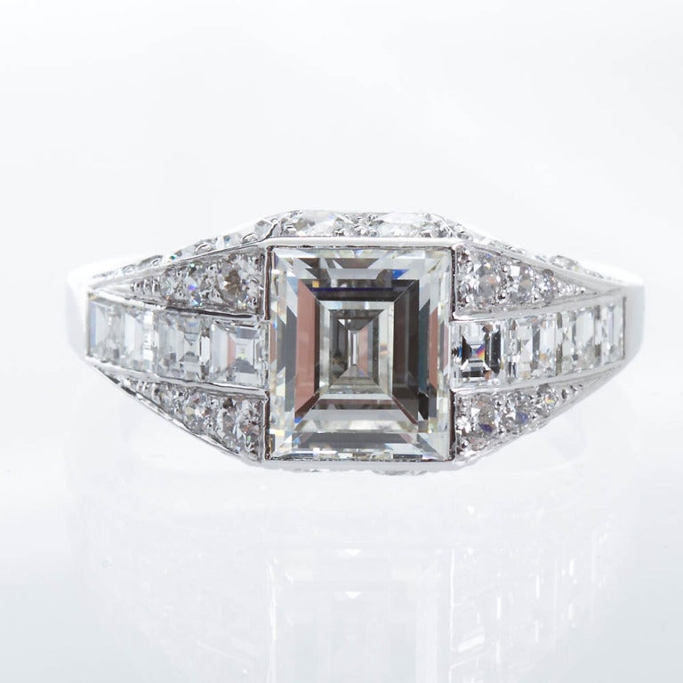 Art Deco ring has a ~2.00 carat square step cut center stone of I color and VVS2-VS1 clarity in platinum. There is another approximately 2.40 carats of diamonds of square cuts and round brilliant cuts on the side and on the profile of the ring
