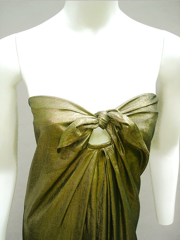 This Gorgeous Metallic Gold Lamé Dress can probably be attributed to Halston 
In the past we have sold a Halston dress in White Jersey in THE Exact same cut and design, and we have had a couple of Halston Dresses with this exact Gold Lame Fabric.