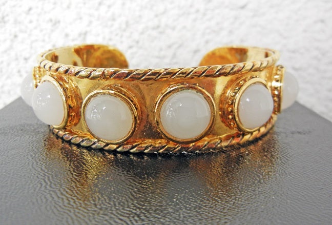 Chanel Baroque style slender cuff bracelet beautifully and elegantly crafted in gold metal with braided trim.   The ten (10) bezel set glass cabochons similiar in color to moonstone or chalcedony.  Signed.

Approx 3/4