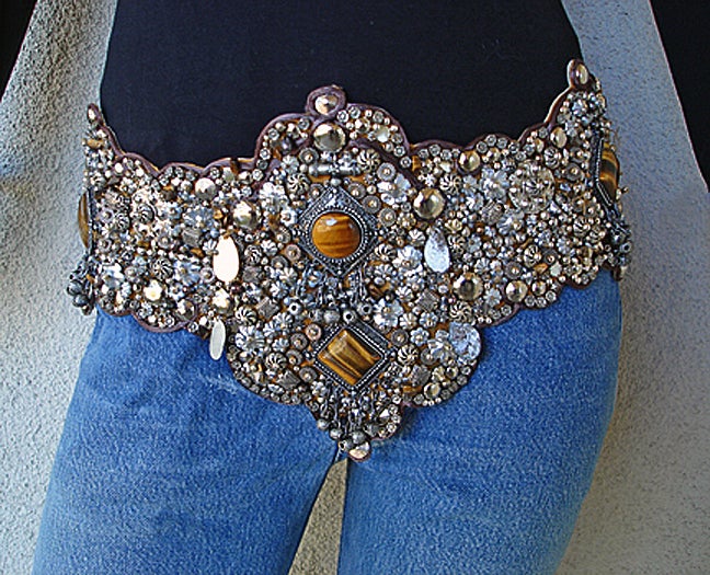 As seen on the runway, exotic with an ethnic flavor a special Oscar de la Renta belt fashioned on a ground of genuine ostrich skin overlayed in encrusted layers of tiny silver metal grommets, flowers, wheels and hanging metal teardrops. Prominently