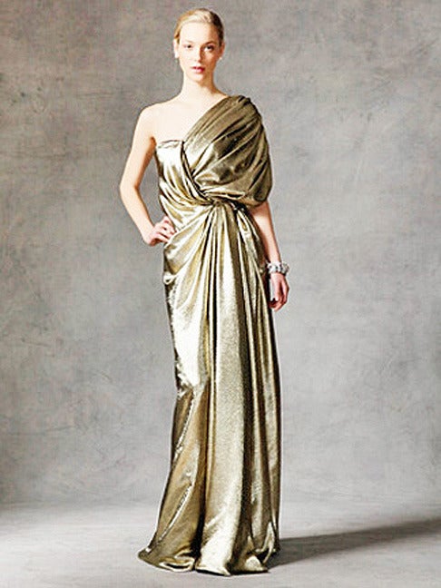 Reem Acra's grecian goddess liquid gold gown. Expertly and dramatically draped in silk gold lame. Boasts one-shoulder style, shirring at shoulder, crossover draped panels at bodice, gathered at front waist and finished with draped panels at skirt.