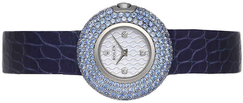 This stunning watch features an 18k white gold case, with a large bezel set with 141 sky blue sapphires. The Rolex mother of pearl dial has 4 diamond hour markers. The blue strap band has an 18k white gold buckle set with 86 sky blue sapphires. It