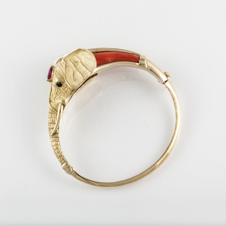 Elephant bangle bracelet composed of 18K yellow gold with coral and accented by blue sapphires, diamonds and a ruby.  The diamonds total 0.55 carats.