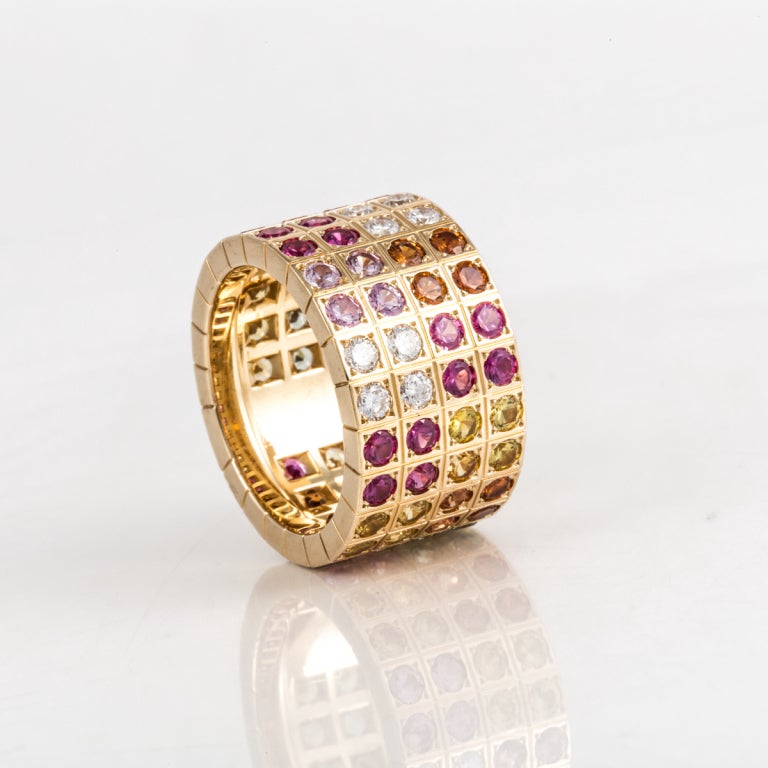 This wide 18k yellow gold band is made by Cartier. It has 8 round brilliant-cut diamonds that weigh 0.50 carats total weight, and 76 round brilliant-cut multi-colored sapphires that weigh 9.85 carats total weight. The ring is size 7.25, but has a