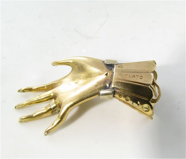 A Paul Flato 18 karat yellow gold, platinum and diamond “Hand and Glove” pendant charm.  Circa 1940’s.  Signed FLATO.  The pendant is realistically modeled as a hand in a lace cuffed glove with a platinum set diamond ring and platinum and diamond