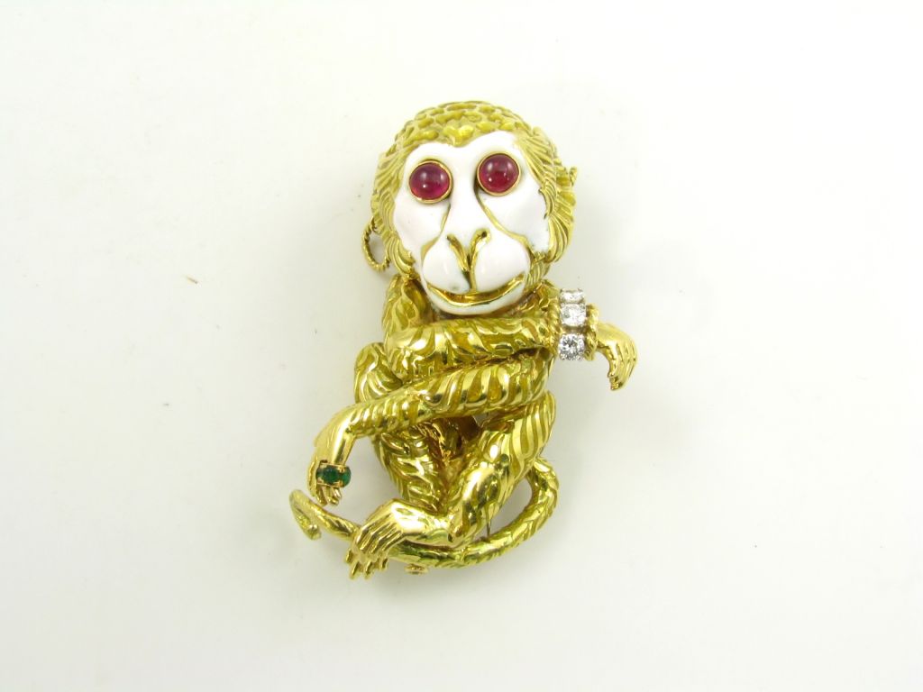 An 18 karat yellow gold, white enamel, ruby, diamond and emerald monkey brooch.  Signed David Webb.