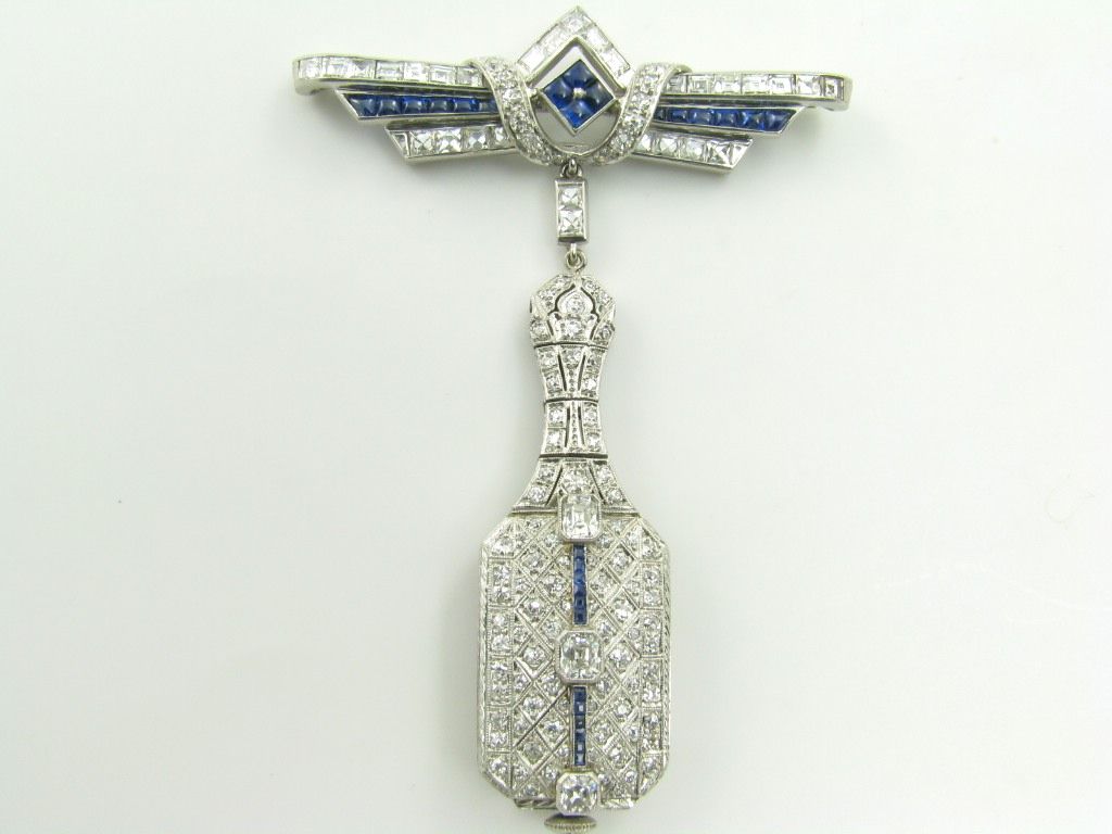 An Art Deco, platinum, sapphire and diamond lapel watch.  Formerly party from Geraldine Farrar.  Signed Grant A. Peacock.  With three (3) emerald cut diamonds approximate weight .80 carats, twenty nine (29) square and french cut diamonds approximate