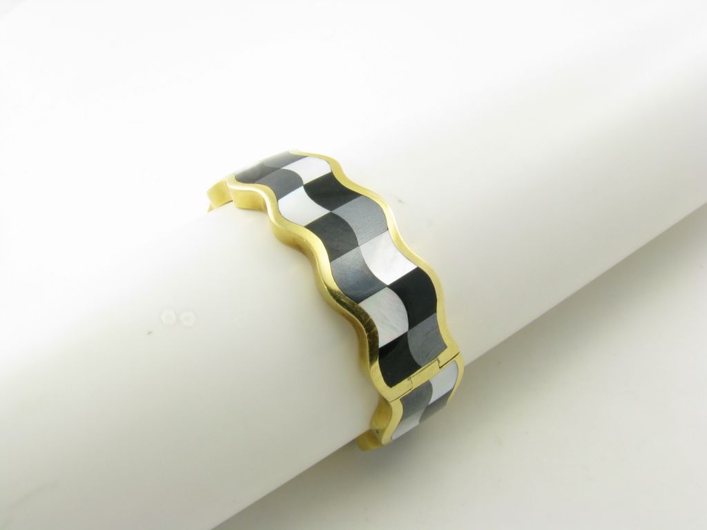 An 18 karat yellow gold, mother of pearl, hematite, and black onyx bracelet.  Signed Tiffany and Company.  Circa 1980’s.  Designed as a hinged bangle bracelet with a checker board design of alternating mother of pearl, black onyx and hematite. 