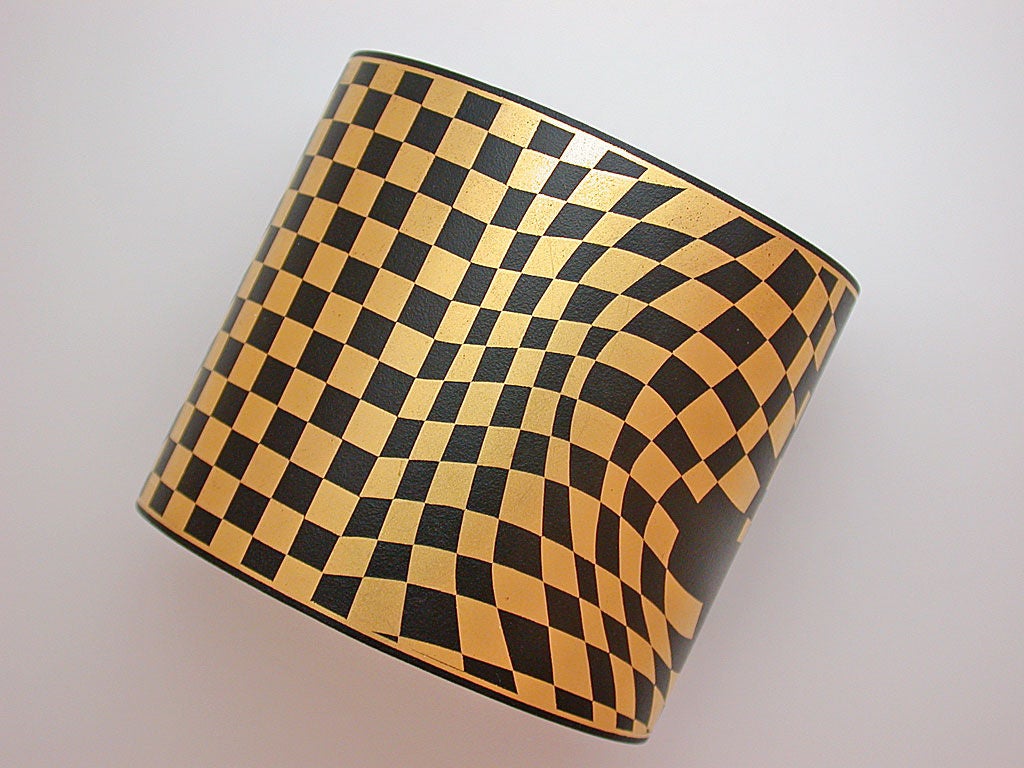 Open bangle of twenty-four karat gold and black lacquered iron, in a graphic checkerboard pattern, predominantly darker moving toward the back edges, lined with gold. Designed by Angela Cummings in Damascene, the ancient jewelry technique of