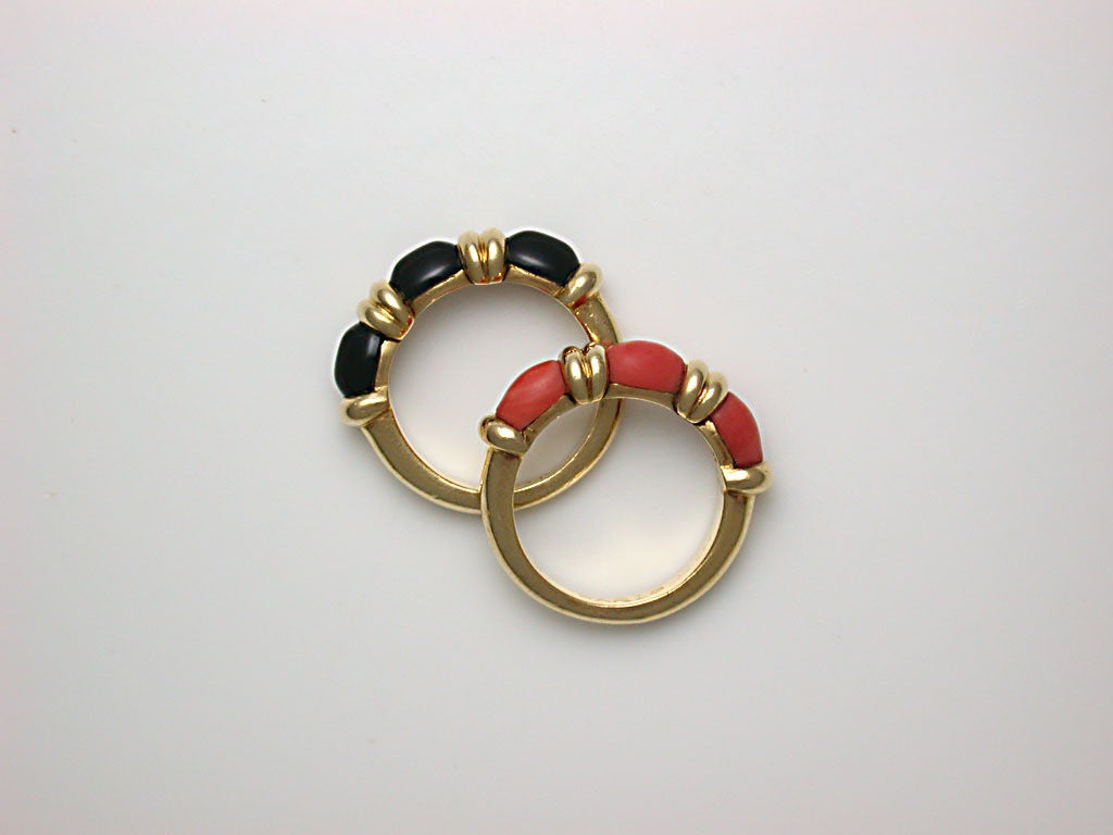 A charming pair of narrow, polished yellow gold band rings, one accented across the top with three cabochon orange coral stones, the other similarly decorated with black onyx, signed HERMES PARIS, numbered #52236 and #52277, fit finger size 4 3/4,
