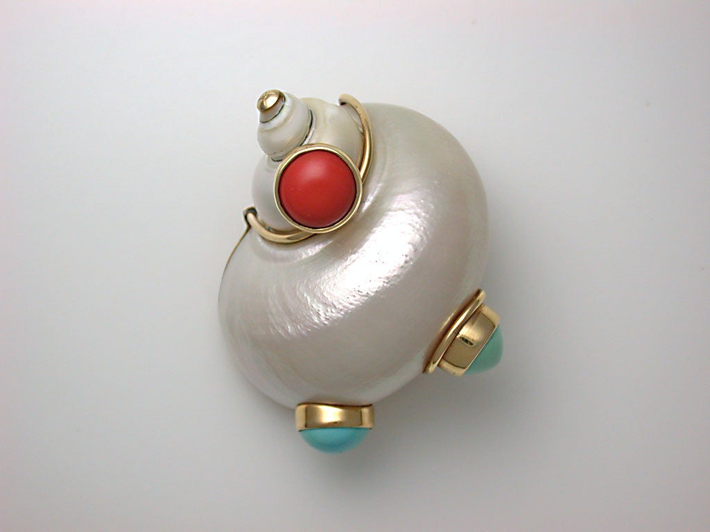 The pearly-white turbo shell wrapped with gold wire and studded with deep orange coral, pale turquoise and vibrant turquoise cabochons, with gold cap at top, signed SEAMAN SCHEPPS, stamped 14K, ca. 1940.