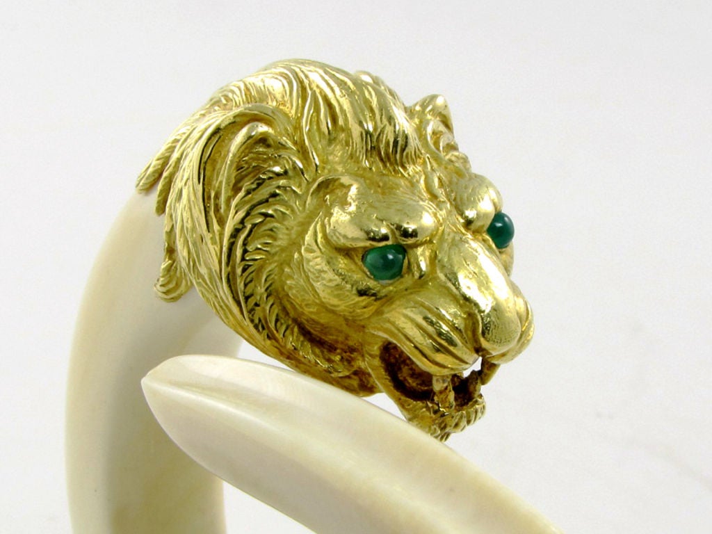 The exotic, carved ivory bangle hinged at the base, with confronting lion's head and tusk motifs at the top, set with cabochon green onyx eyes, signed VCA for Van Cleef & Arpels, Paris, numbered #127865, with French assay marks for 18kt gold, circa