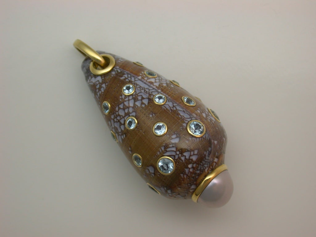 The natural shell pendant colored medium brown with pale blue/grey mottling, set at the tip with a white South Sea baroque half pearl, accented with blue topaz spots,  mounted in 18kt yellow gold, hallmarked for Trianon.