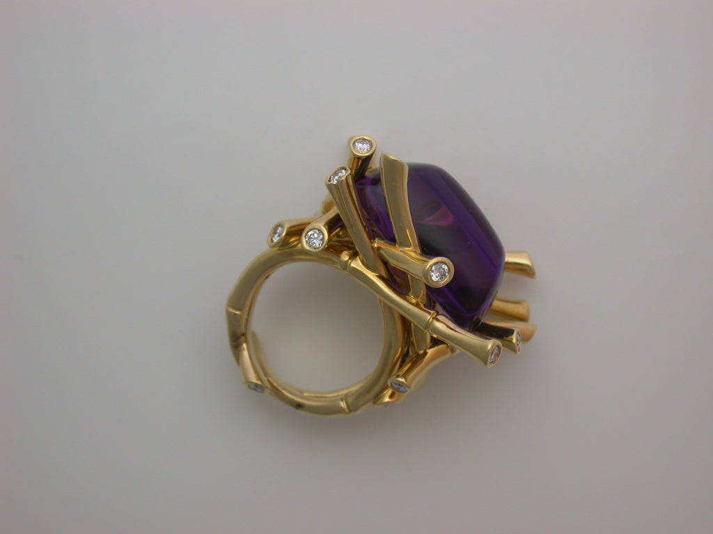 The large, oblong sugarloaf cabochon amethyst quartz (a bright, clean stone weighing approximately 26.52 carats) set across the finger within a dramatic nest of polished yellow gold bamboo canes set at the tips with white diamonds, woven bamboo